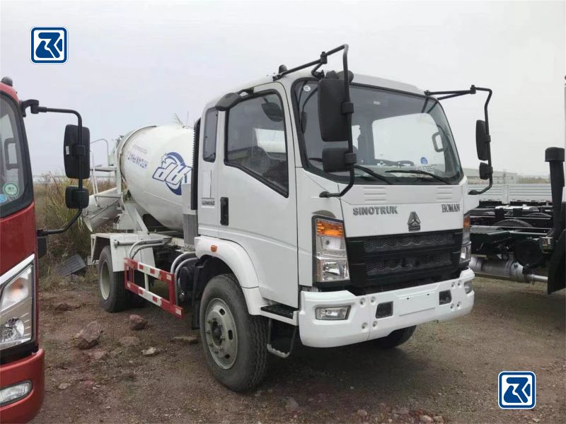 Vista lateral de um camião betoneira HOWO 4x2 branco estacionado num terreno de gravilha, mostrando a cabina do condutor e o tambor cilíndrico da betoneira com a marca da empresa.